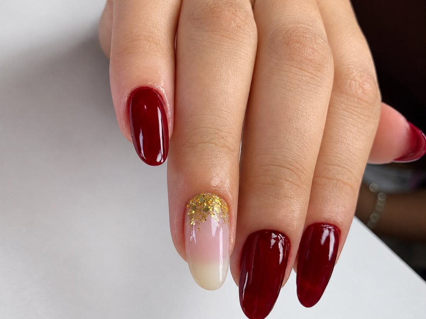 Unhas em vermelho bordo com detalhe dourado, feitas na Laviance